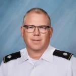 Man in military uniform with glasses, smiling.