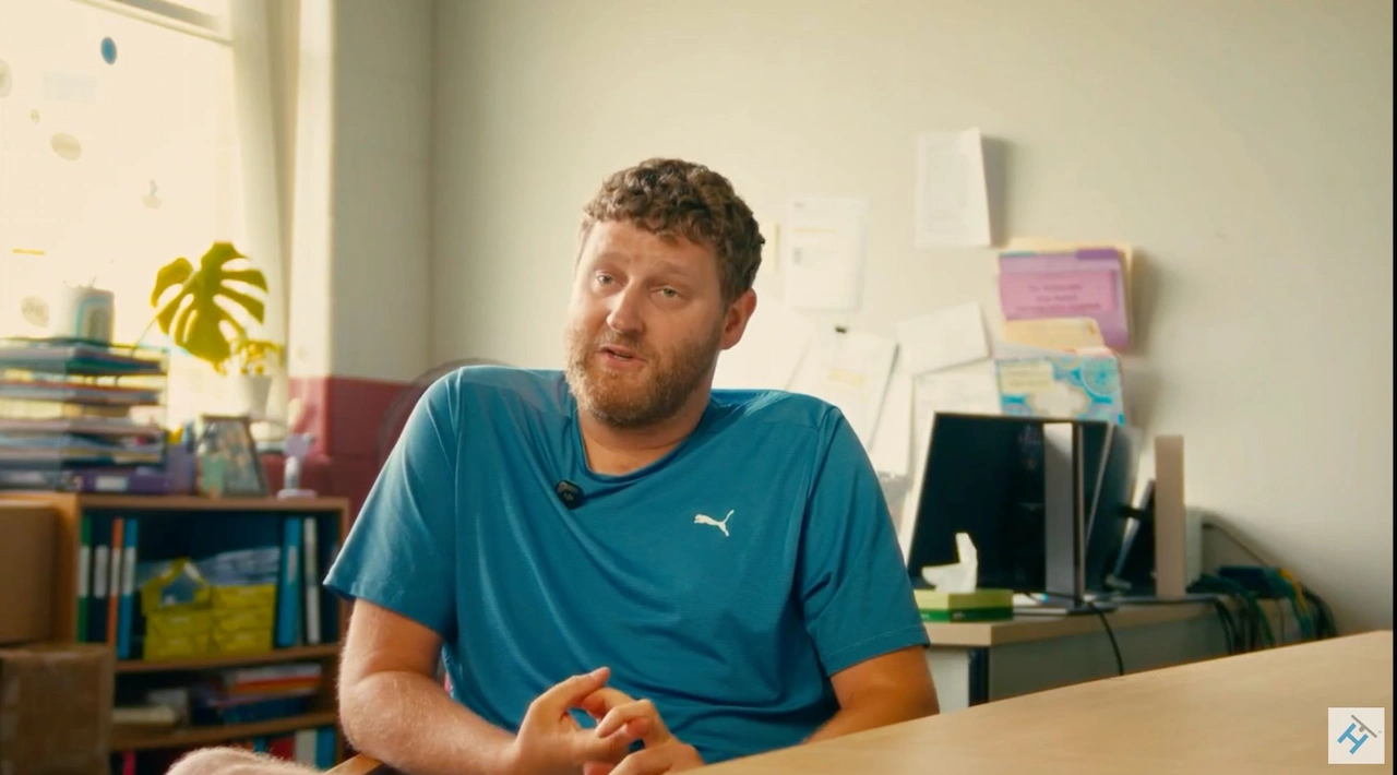 Man in blue shirt sitting at office desk.