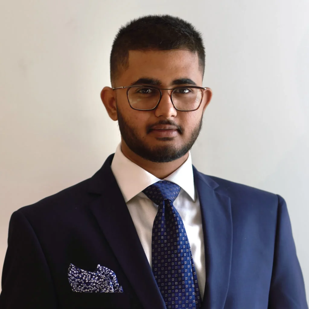Man in navy suit with glasses smiling.