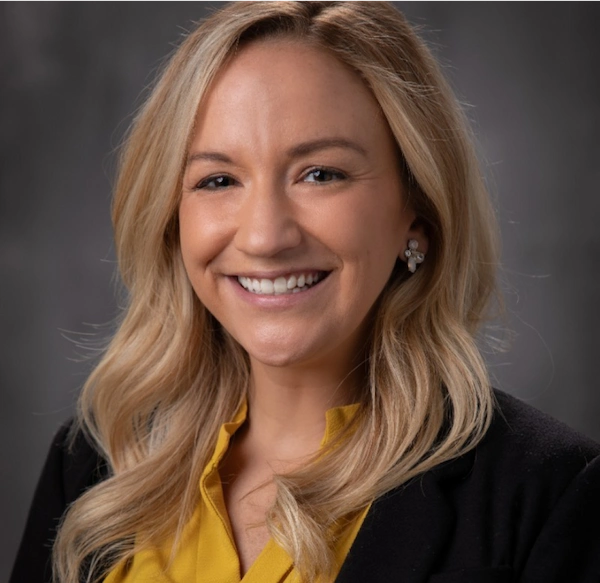 Smiling person with blond hair and black blazer.