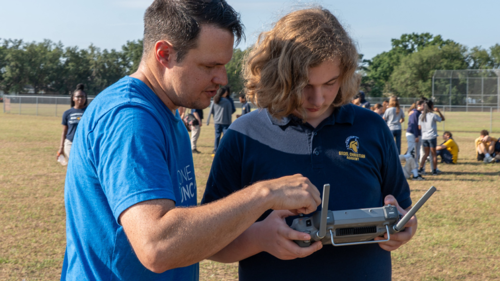 Instructor teaching student to operate drone controller.