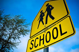 Yellow school crossing sign with blue sky.