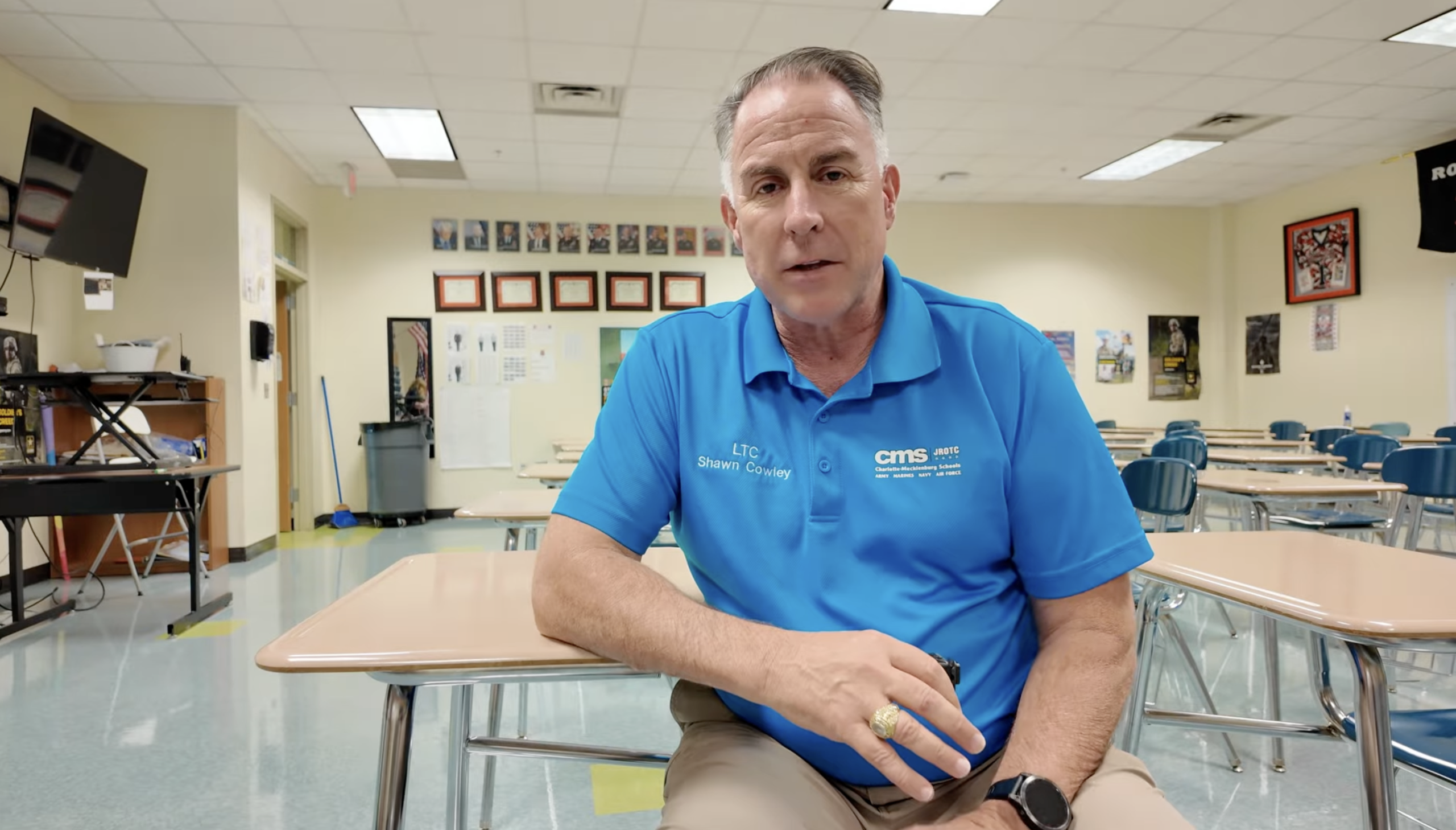 Man in classroom with empty desks behind him.